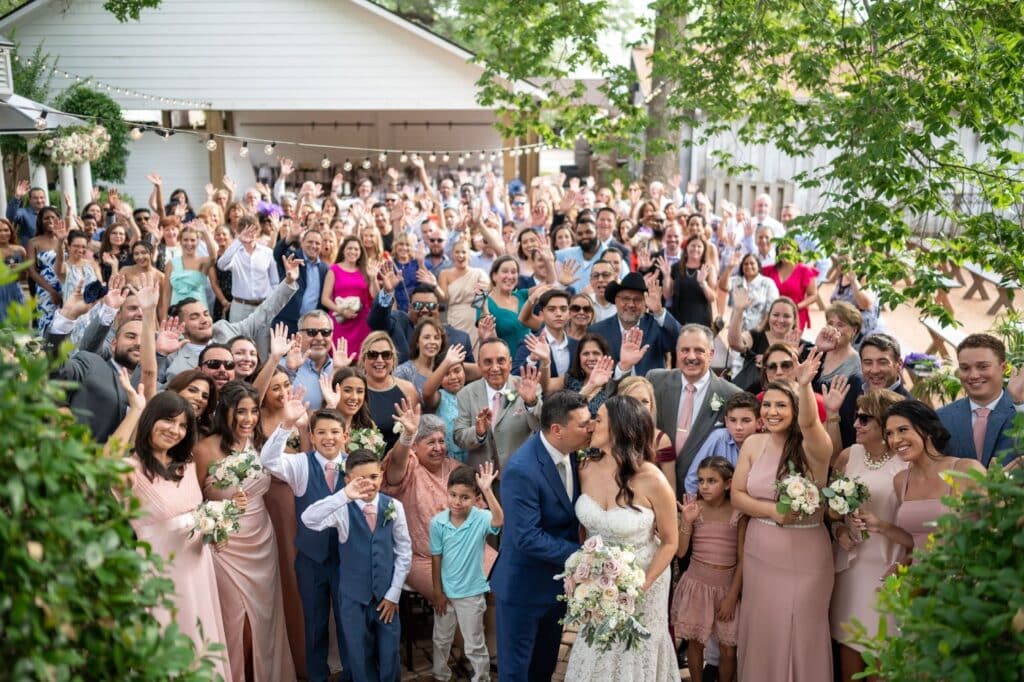 At Butler's Courtyard near Houston Texas, a group shot of all the wedding attendees with bride and groom kissing in the center. 