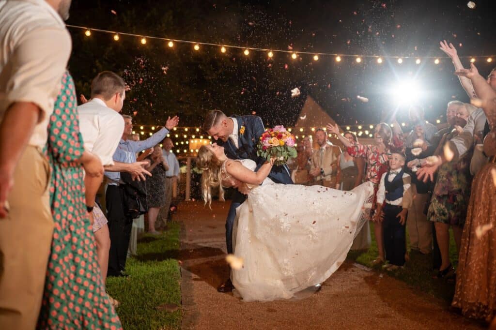 Grand exit from reception at Butler's Courtyard an all-inclusive wedding venue in Houston Texas. Guests throwing lavender and rose petals like confetti, groom dips bride for a kiss.