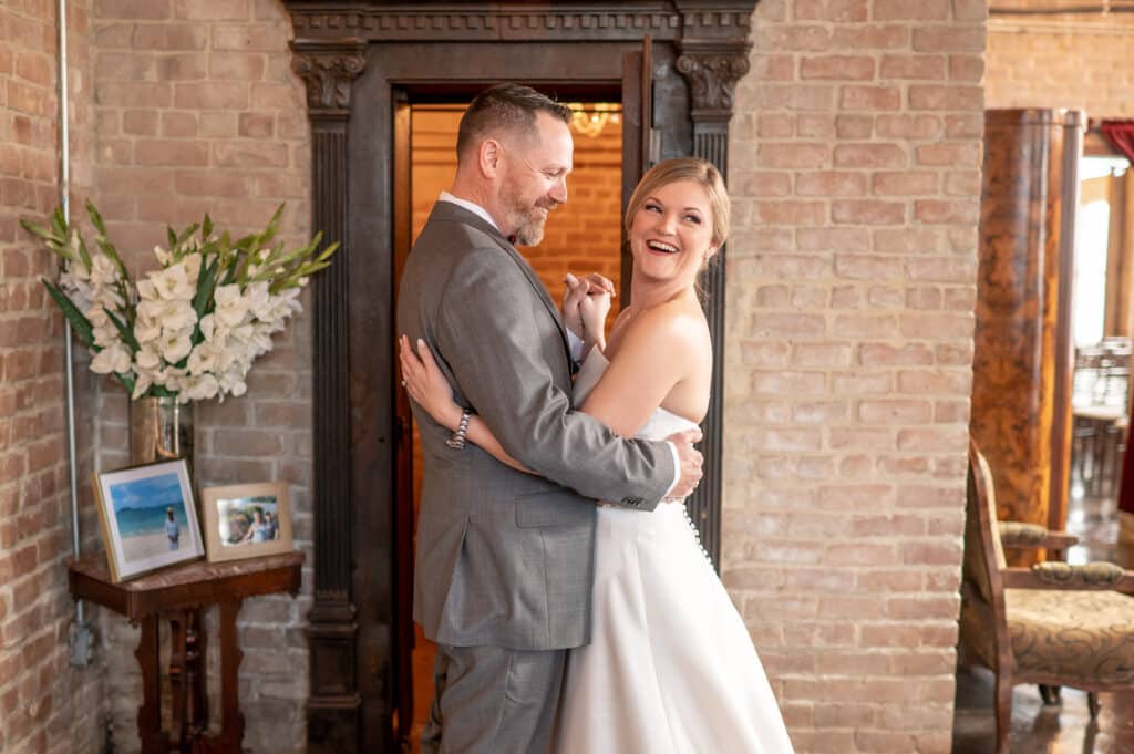 Smiling bride and groom share a quick dance at Butler's Courtyard a historic wedding venue near Houston Texas. They’re surrounded by bricks and behind them is a one of a kind metal vault door.