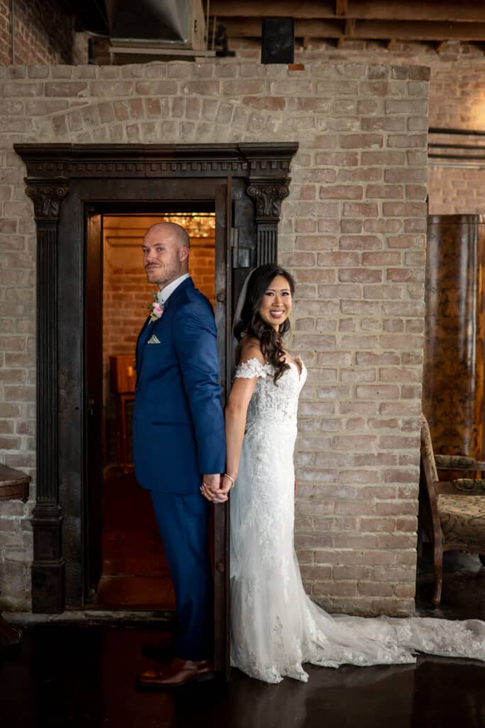 Bride and groom share their first touch at Butler's Courtyard around the historic metal bank vault door surrounded by the charming brick, highlighting 2025 Wedding Trends and the charm of a Historic Wedding Venue.