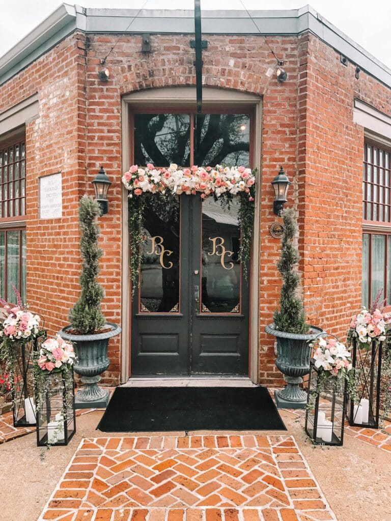 The front doors of Butler’s Courtyard, a historic brick building in League City, Texas, recognized as a local landmark, adorned with pink and white wedding flowers.