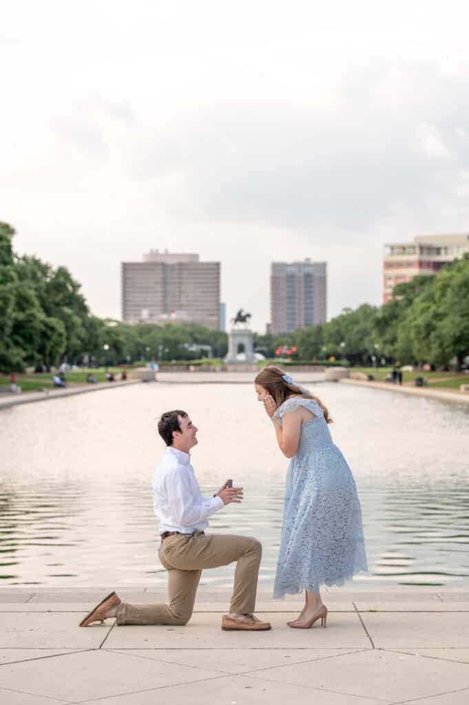 Guy down on one knee proposing to an excited lady at a popular Houston Park with the skyline behind them 