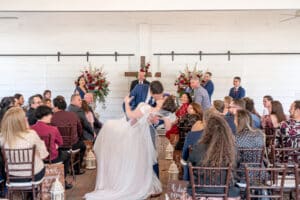 Groom romantically dips his bride for a kiss at the end of the aisle at Butler's Courtyard, surrounded by joyful friends and family under the venue's charming outdoor wedding pavilion.