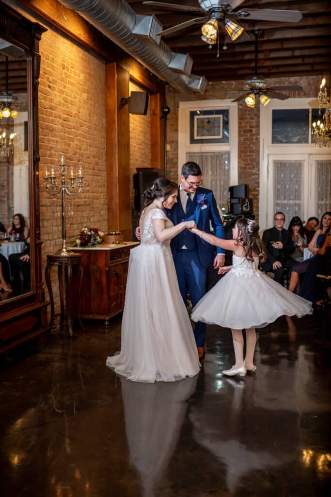 Bride and Groom share a special dance with their daughter. Her dress opens as she twirls around the dance floor surrounded by family and friends. 