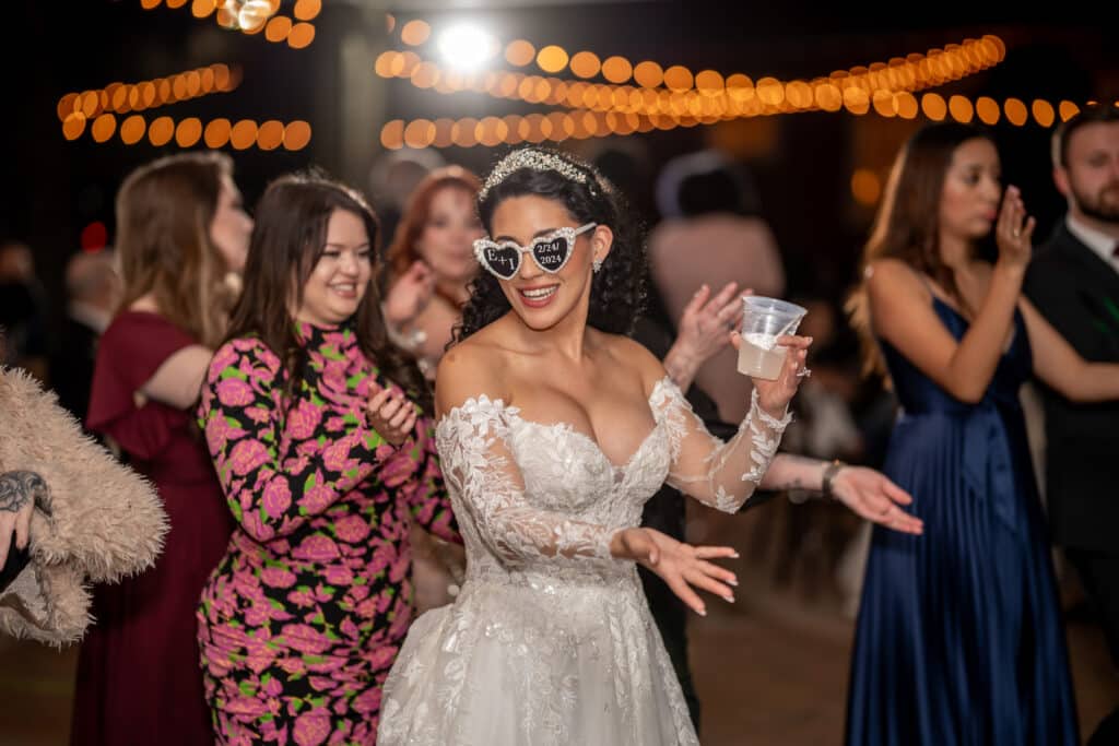 Bride wearing custom sunglasses does the macarena on the dance floor during her Houston Texas Wedding Reception at Butler's Courtyard