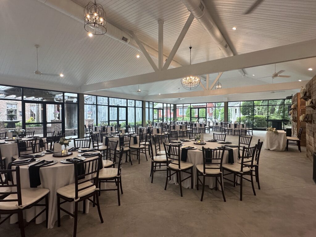 Bright white ballroom with two window walls offering beautiful views of Butler's Courtyard's many unique historic buildings and sparkling courtyard string lights.