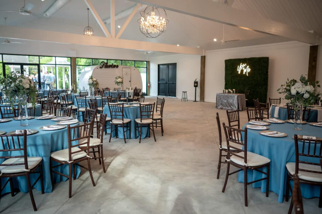 Elegant wedding ballroom featuring a lush greenery wall backdrop, sparkling crystal chandeliers, and the charming gingersnap photo camper, creating a modern and luxurious event space.