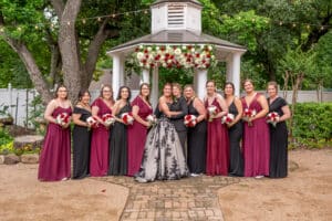 Two brides, one in a stunning black wedding dress, celebrating with their wedding party at Butler's Courtyard, a premier Houston wedding venue.